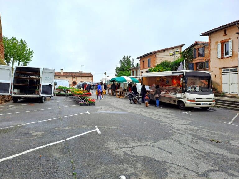 Marché en plein air avec camions de vente et étals de produits locaux sur une place de village